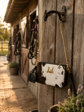 Loyal West Shell Mini Purse in black and white cowhide hanging on stable door with gold chain strap and horseshoe charm
