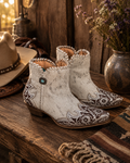 Sierra Belle handtooled leather booties in almond white showing floral tooled toe cap and turquoise concho on rustic wooden surface